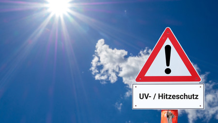 Blauer Himmel mit gleißender Sonne und Warnschild mit Text "UV-/Hitzeschutz